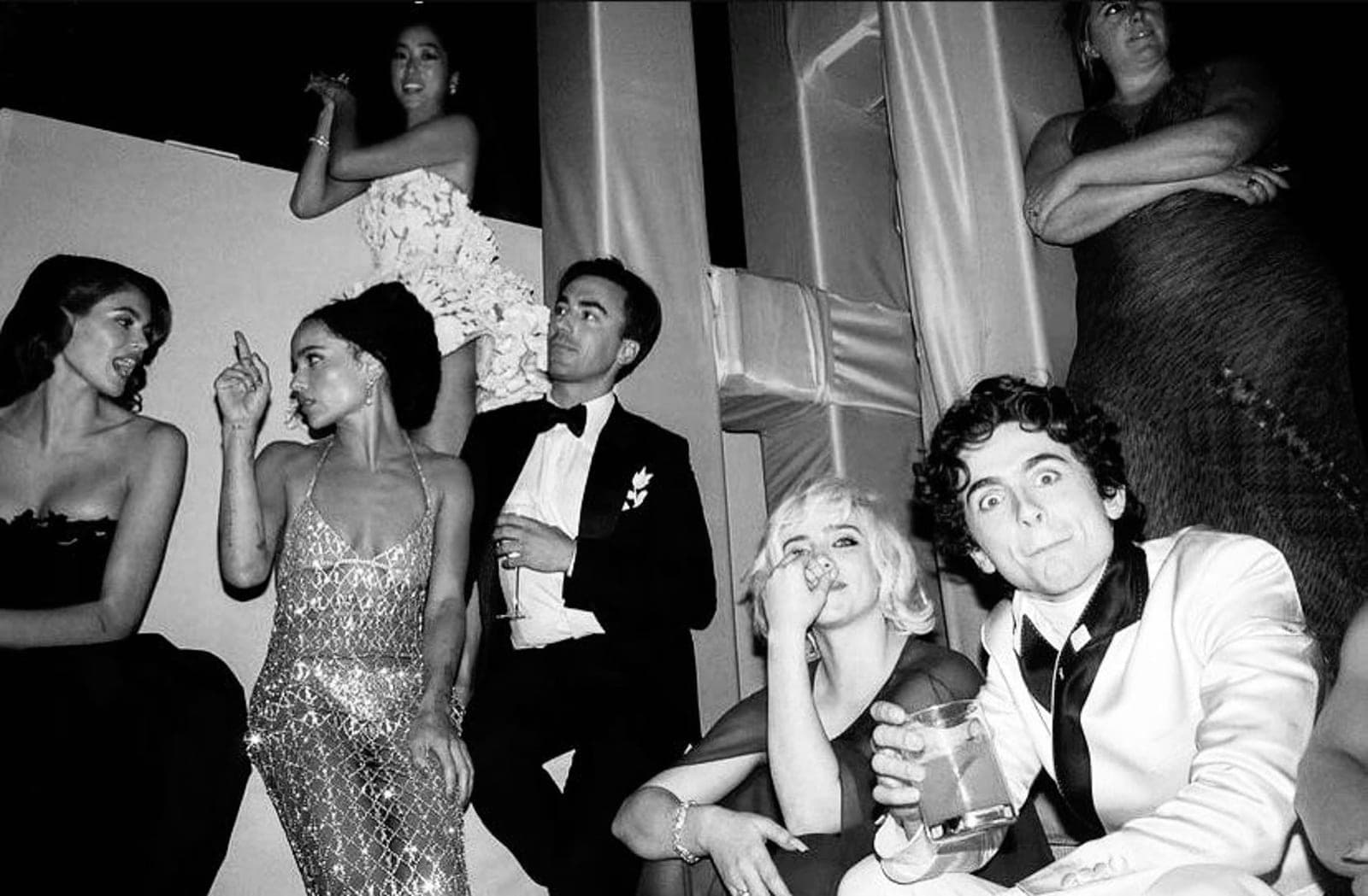 A black-and-white photograph of a gala. Friends in evening wear, candid mid-laugh.